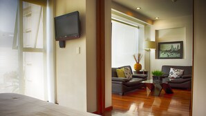 A modern hotel room with a large bed, a flat-screen TV mounted on the wall, a sofa, a coffee table, and a framed picture on the wall. - Aura For Living (Mexico City)