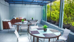 A modern indoor patio area with round tables and chairs, potted plants, and a buffet setup. - Aura For Living (Mexico City)