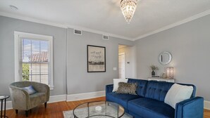 Een woonkamer met een blauwe bank, een grijze fauteuil, een glazen salontafel en een kroonluchter.