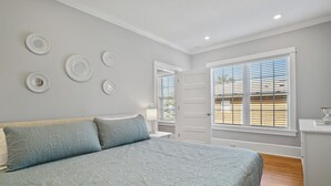 Een slaapkamer met een bed, nachtkastje, dressoir en een raam met jaloezieën.