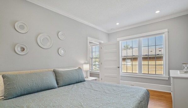 Een slaapkamer met een bed, nachtkastje, dressoir en een raam met jaloezieën.