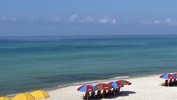 Una playa con arena blanca, agua cristalina y varias sombrillas.