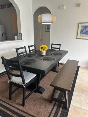 Un comedor con una mesa rectangular, seis sillas, un banco, una lámpara colgante y un cuadro en la pared.