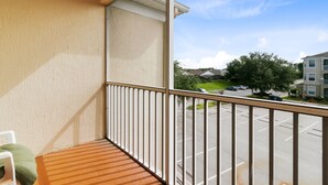 Ein Balkon mit Holzboden und weißem Geländer, mit Blick auf einen Parkplatz und Wohnhäuser.