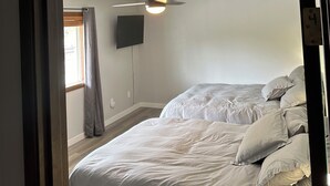 Quarto com duas camas, ventilador de teto e televisão na parede.