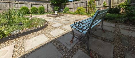 Een terras met een stenen pad, een houten hek en een bank.