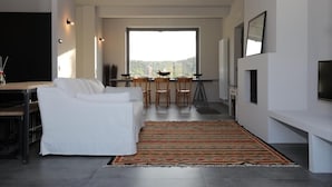 A modern living room with a white sofa, a dining area with chairs, a large window, and a TV on the wall. - Casa Adele 1 per una Vacanza in Semplicità e Relax (Itri)