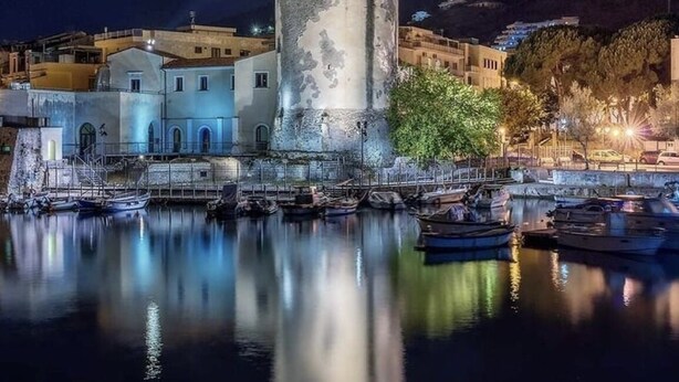 A historic tower with a cylindrical base and a crenellated top, surrounded by calm water reflecting the structure. - Casa Adele 1 per una Vacanza in Semplicità e Relax (Itri)