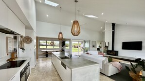 A modern kitchen with a central island, large windows, and a dining area with a bench. - Coastal Retreat - POOL,  SPA & FIRE. Nature boardwalk, creek & inlet. 5 bedroom. (Inverloch)