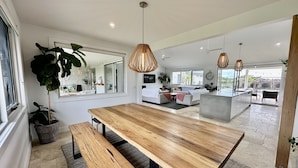 A modern kitchen with a large wooden table, hanging pendant lights, and a view of the backyard. - Coastal Retreat - POOL,  SPA & FIRE. Nature boardwalk, creek & inlet. 5 bedroom. (Inverloch)
