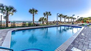 A swimming pool with a tiled deck, palm trees, and a clear sky. - 5-Star Luxury, Fully Updated OCEANFRONT 2 Bed/ 2 Bath FALL STAYS 50% OFF RESORT! (Myrtle Beach)