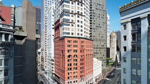 A high-rise building with a red facade and large windows, surrounded by taller buildings.