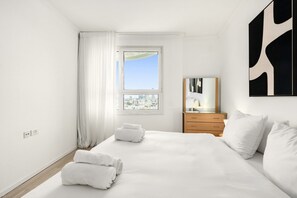 Une chambre d’hôtel avec un grand lit, une table de chevet, un miroir et une vue sur le paysage urbain par la fenêtre.