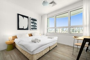 A modern hotel room with a large bed, a desk, and a view of the city.