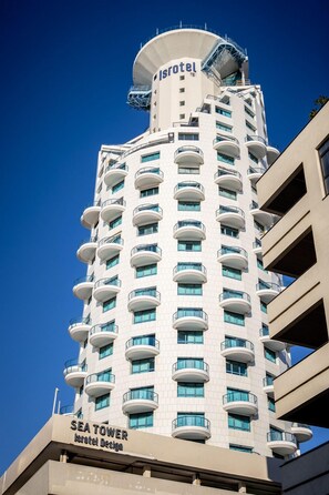 Un grand hôtel avec une partie supérieure cylindrique, des balcons et une enseigne indiquant « SEA TOWER Isotel Design ».