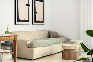 Un salon aux couleurs neutres, avec un canapé, une petite table en bois et deux œuvres d’art abstraites encadrées accrochées au mur.