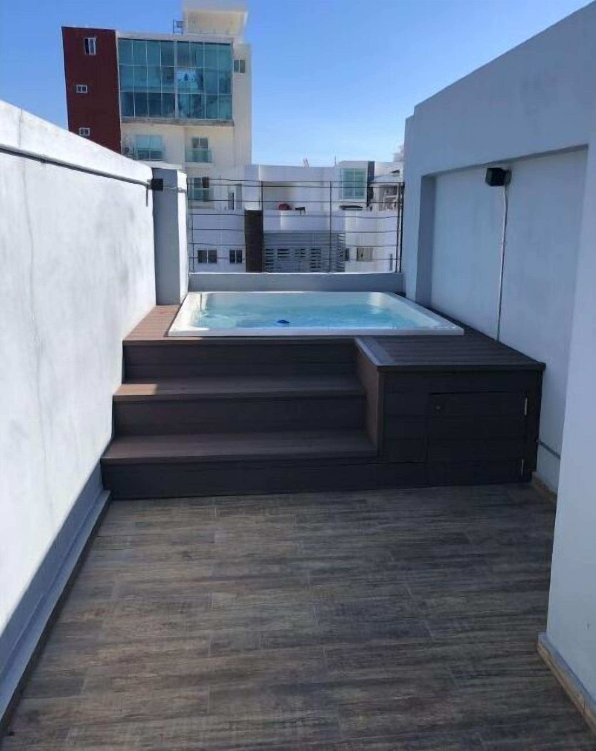 Terraza con jacuzzi, escaleras de madera y vistas de edificios circundantes.