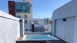Una terrazza sul tetto con vasca idromassaggio, scale in legno e vista sugli edifici circostanti.