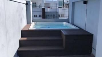 Terraza con jacuzzi, escaleras de madera y vistas de edificios circundantes.