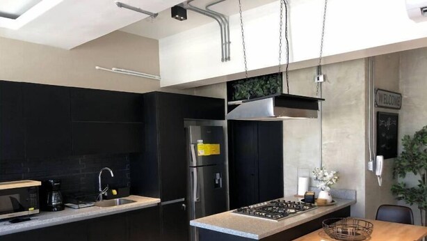 Una cucina moderna con mobili scuri, un frigorifero in acciaio inossidabile, un piano cottura a gas e un tavolo da pranzo in legno.