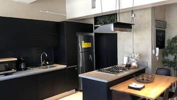 Una cocina moderna con muebles oscuros, un refrigerador de acero inoxidable, una estufa a gas y una mesa de comedor de madera.