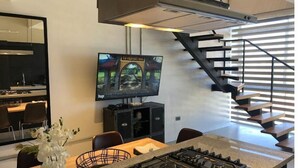 Una cucina moderna con piano cottura a gas, una zona pranzo con sedie, una TV montata a parete e una scala con ringhiera in metallo.
