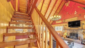 A wooden staircase leading to a living area with a fireplace, television, and various wooden furnishings. - Game Room & 2 Decks: Walkable Lake Arrowhead Cabin (Lake Arrowhead)