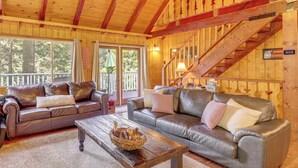 A cozy cabin interior with two leather sofas, a wooden coffee table, and a staircase. - Game Room & 2 Decks: Walkable Lake Arrowhead Cabin (Lake Arrowhead)