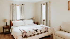 A bedroom with a bed, two bedside tables, a nightstand, a window with curtains, and a sofa.
