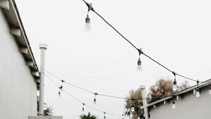 A patio with a wooden table and chairs, string lights, a potted plant, and a decorative tree branch.