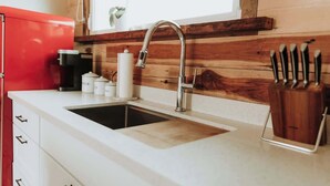 A kitchen with a stainless steel sink, wooden wall paneling, a red appliance, and a knife holder.