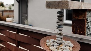 Een stenen constructie met een ronde basis en een verticale stapel stenen, voor een modern huis met een grijze gevel en een bruin hek.