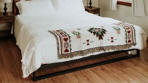 Een slaapkamer met een bed, twee nachtkastjes met lampen, een raam met gordijnen en een schilderij aan de muur.
