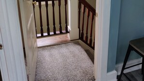 Eine Treppe mit hölzernem Geländer, einem Teppich belagten Podest und einer weißen Tür zu einem Zimmer mit Fenster.