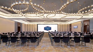 A conference room with rows of tables and chairs, a large screen displaying the Hampton by Hilton logo, and a modern chandelier. - Hampton BY Hilton Qinhuangdao Jinmeng (QINHUANGDAO)