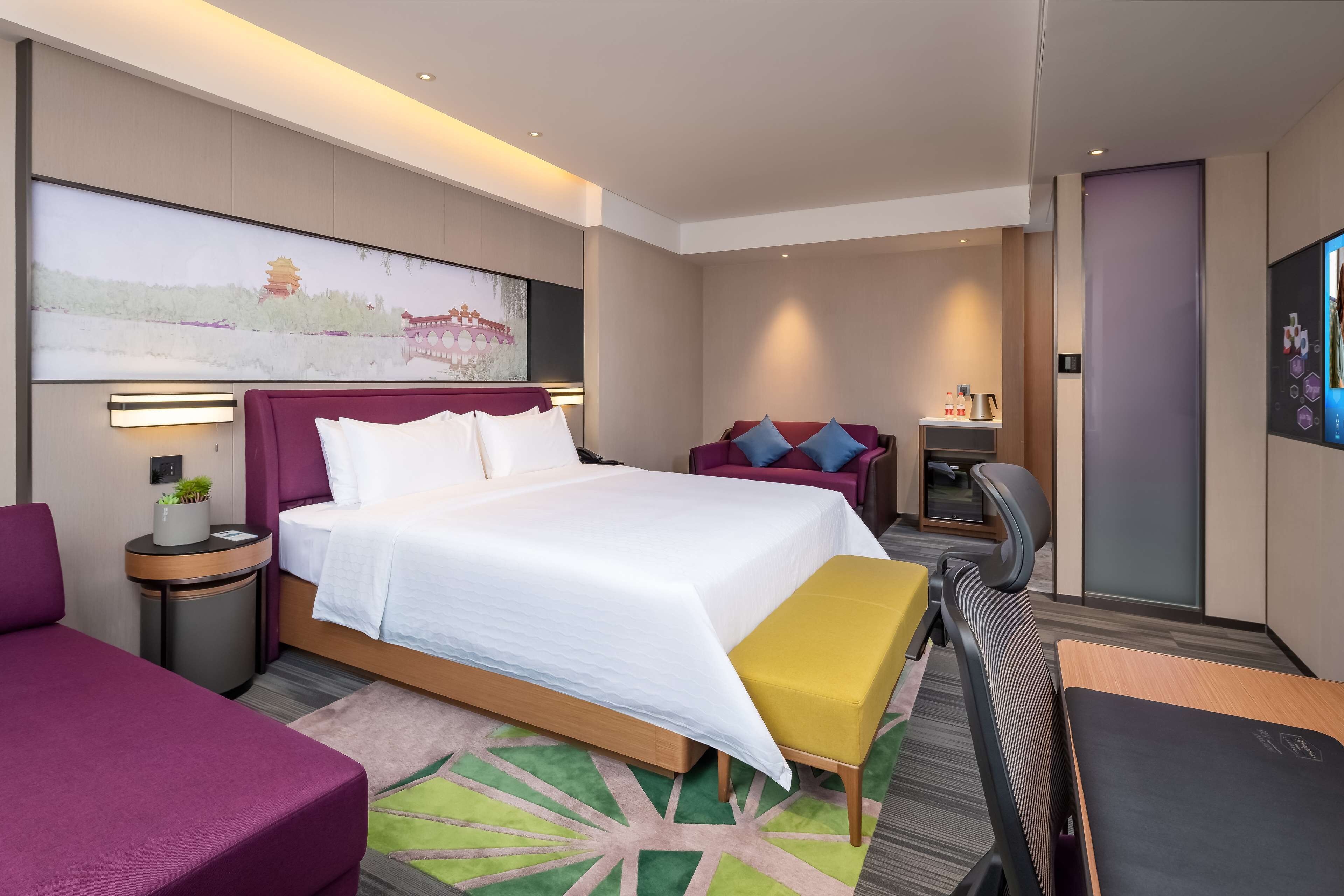 A modern hotel room with a large bed, a desk, a chair, and a TV.