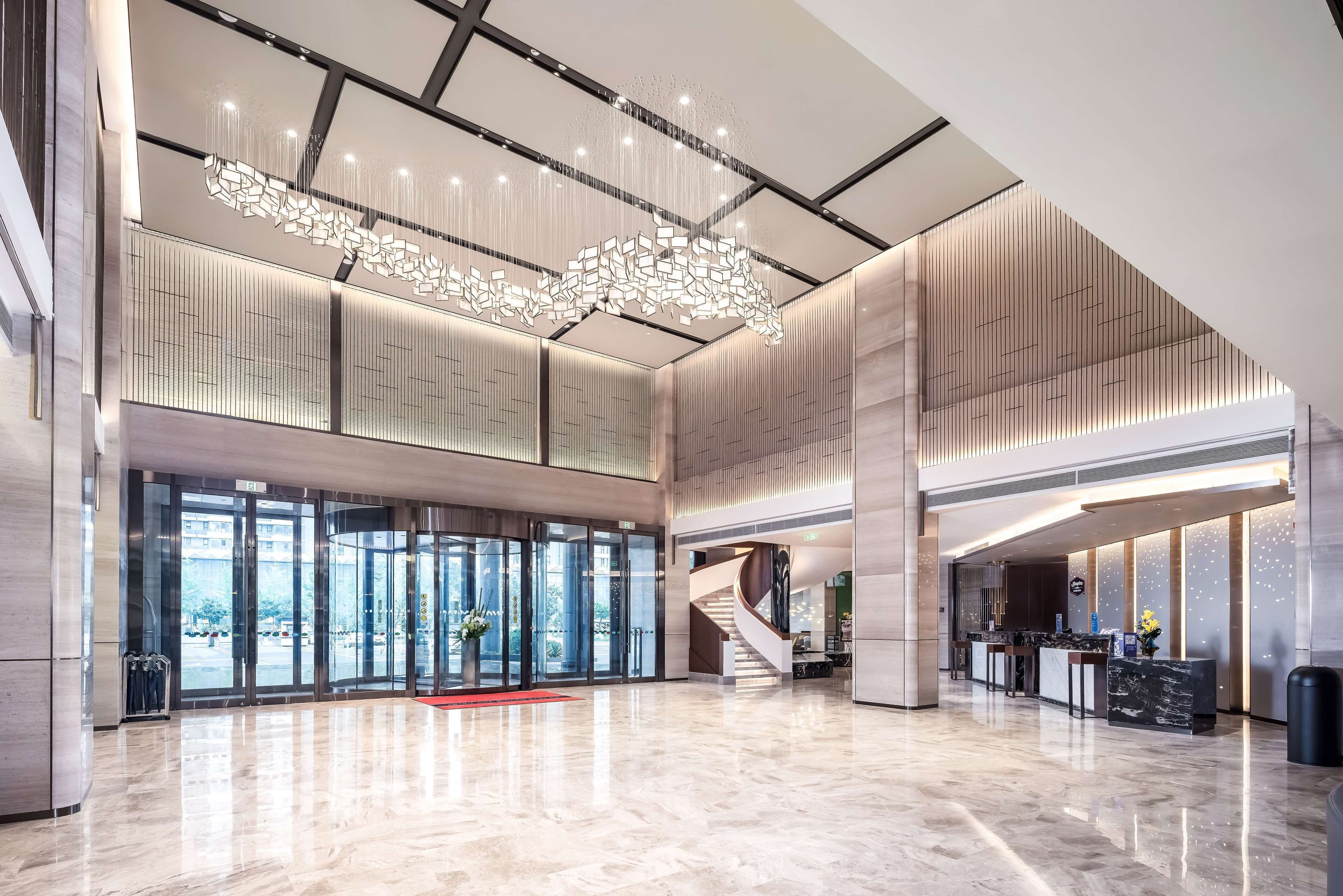 A spacious lobby with a modern chandelier, a reception desk, and a staircase leading to upper floors.