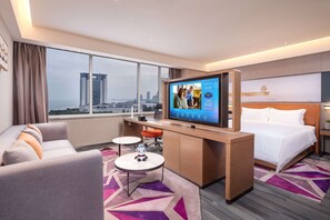 A hotel room with a large TV, a bed, a desk, and a sofa. - Hampton BY Hilton Qinhuangdao Jinmeng (QINHUANGDAO)