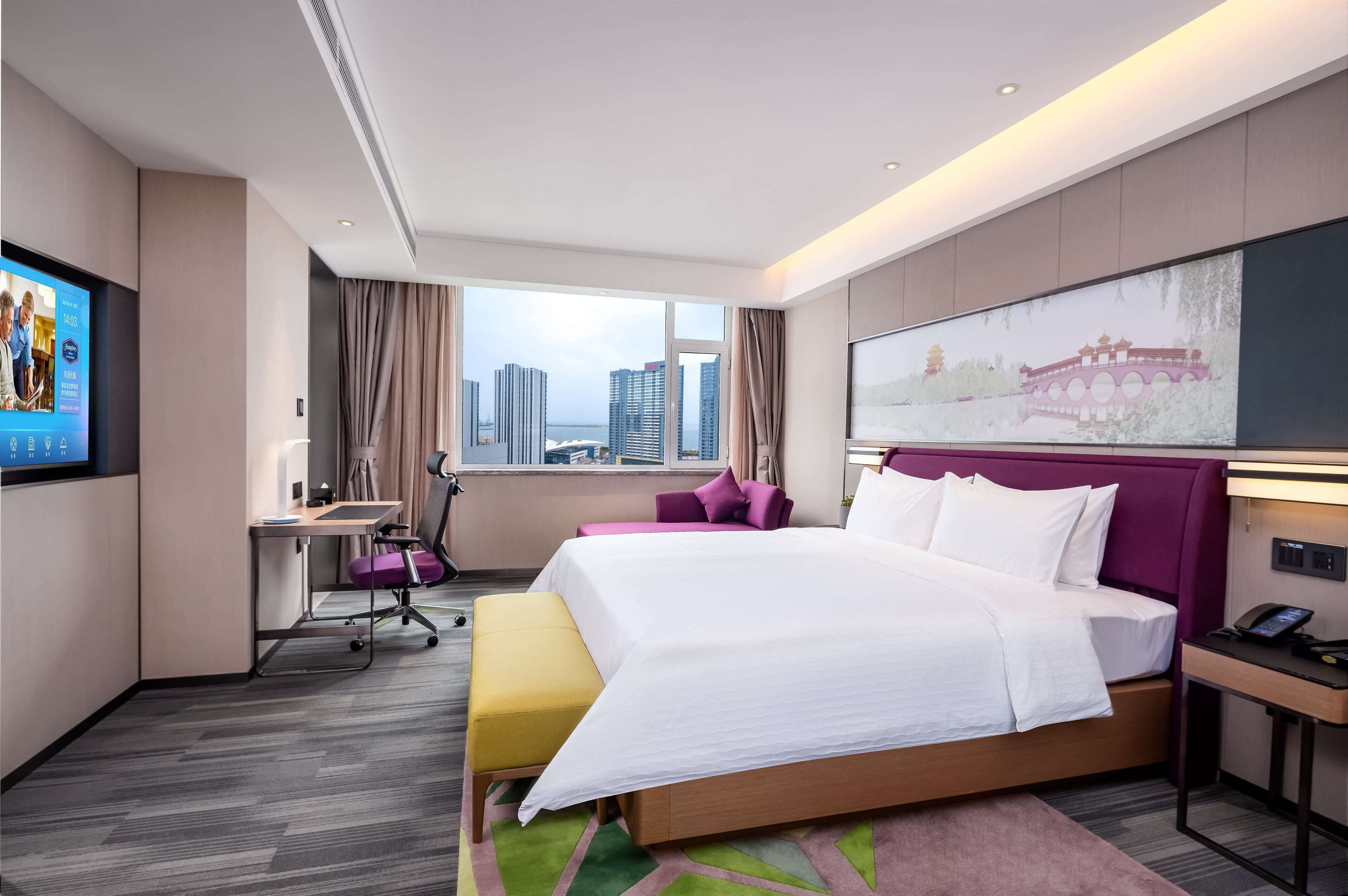 Een moderne hotelkamer met een groot bed, een bureau en uitzicht op de stadshemel.