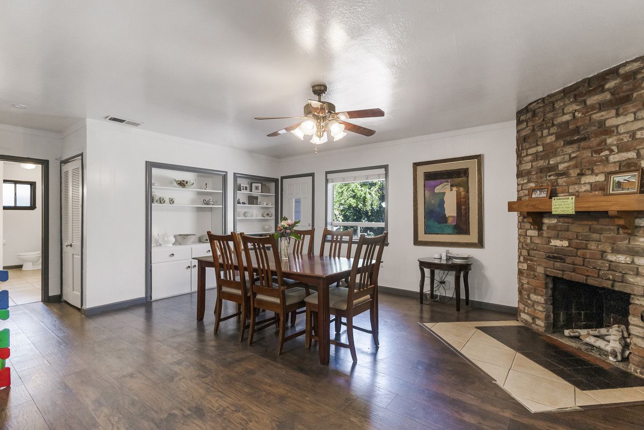 A dining area with a wooden table and chairs, a ceiling fan, and a brick fireplace.
