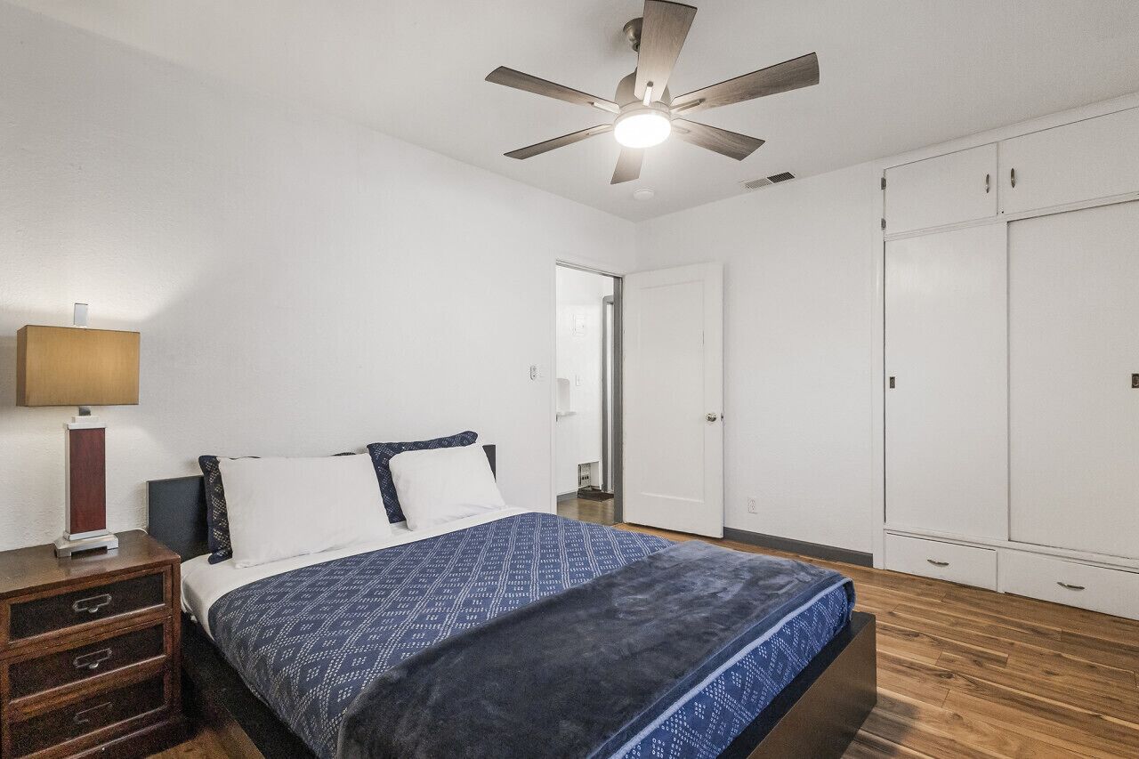 A bedroom with a bed, a nightstand, a ceiling fan, and a wardrobe.