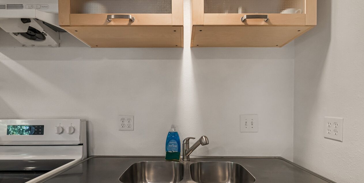 A kitchen with a stainless steel sink, a dish soap dispenser, and a microwave.