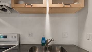 A kitchen with a stainless steel sink, a dish soap dispenser, and a microwave.