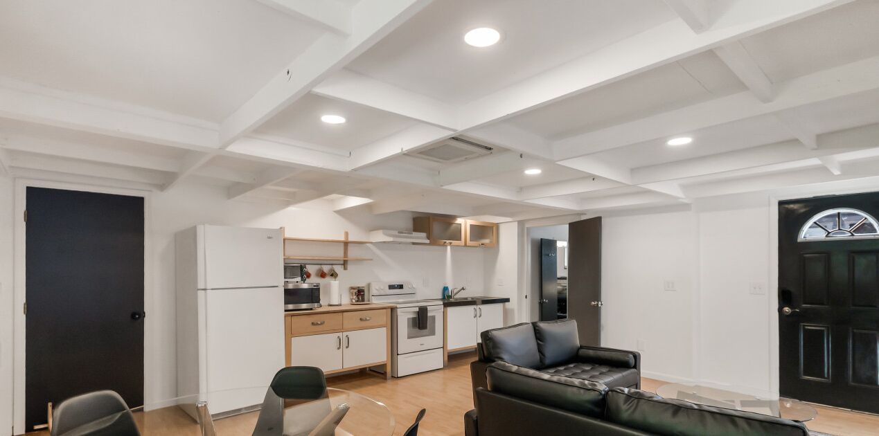 Eine moderne Küche mit weißen Schränken und einer schwarzen Arbeitsplatte, ein Essbereich mit einer schwarzen Ledersofa und eine schwarze Tür mit Fenster.