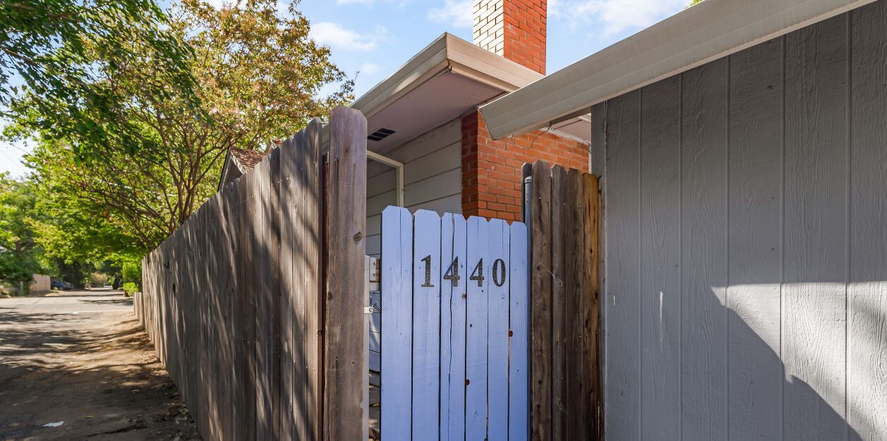 A wooden gate with the number 1440, a brick chimney, and a white door.