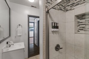 A bathroom with a white sink, a mirror, a towel ring, and a shower with a tiled wall. - Ideal for Families & Groups (Chico)
