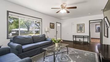 A living room with a dark blue sofa, a glass coffee table, and a ceiling fan.