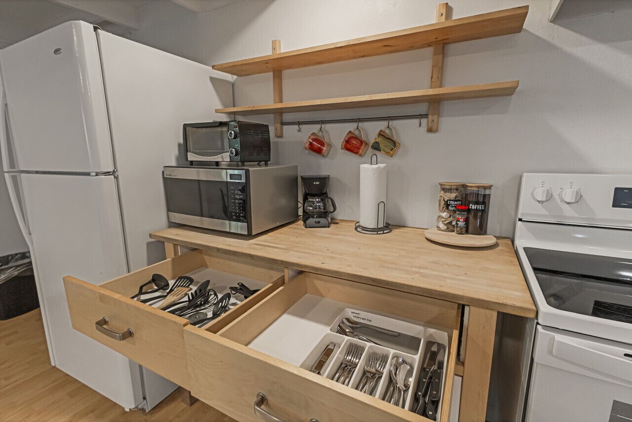 Una cucina compatta con forno a microonde, macchina del caffè e contenitori sul piano di lavoro.