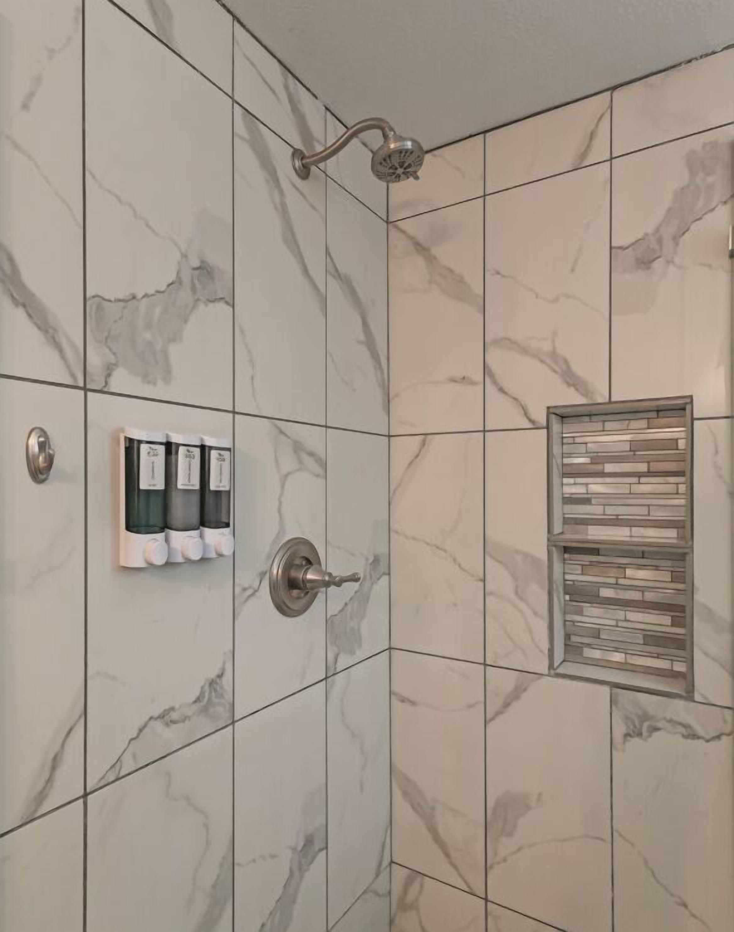 A bathroom with marble tiles, a showerhead, a towel rack with bottles, and a soap dispenser.