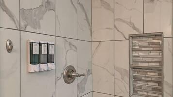 A bathroom with marble tiles, a showerhead, a towel rack with bottles, and a soap dispenser.